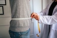 A nutritionist measuring a patient's waist using a tape in a clinical setting.