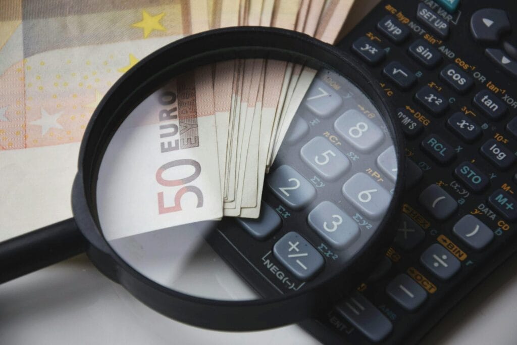 Euro bills under magnifying glass with calculator, symbolizing finance and analysis.