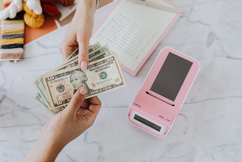 Close-up of hands exchanging US dollars with a pink calculator on a marble surface.